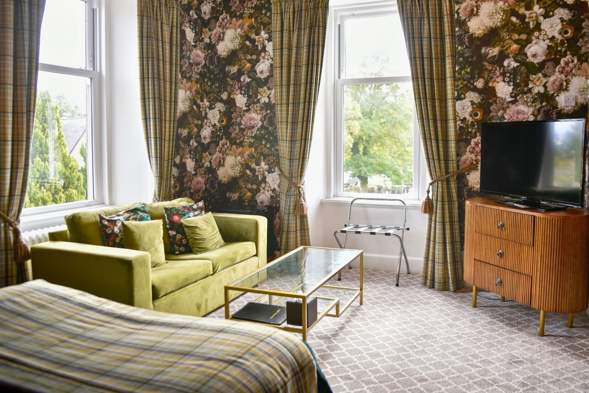 Sofa and coffee table, chest of drawers and tv in executive hotel suite at the Glenesk Hotel. Luxury floral wallpaper and tartan curtains with tie backs,