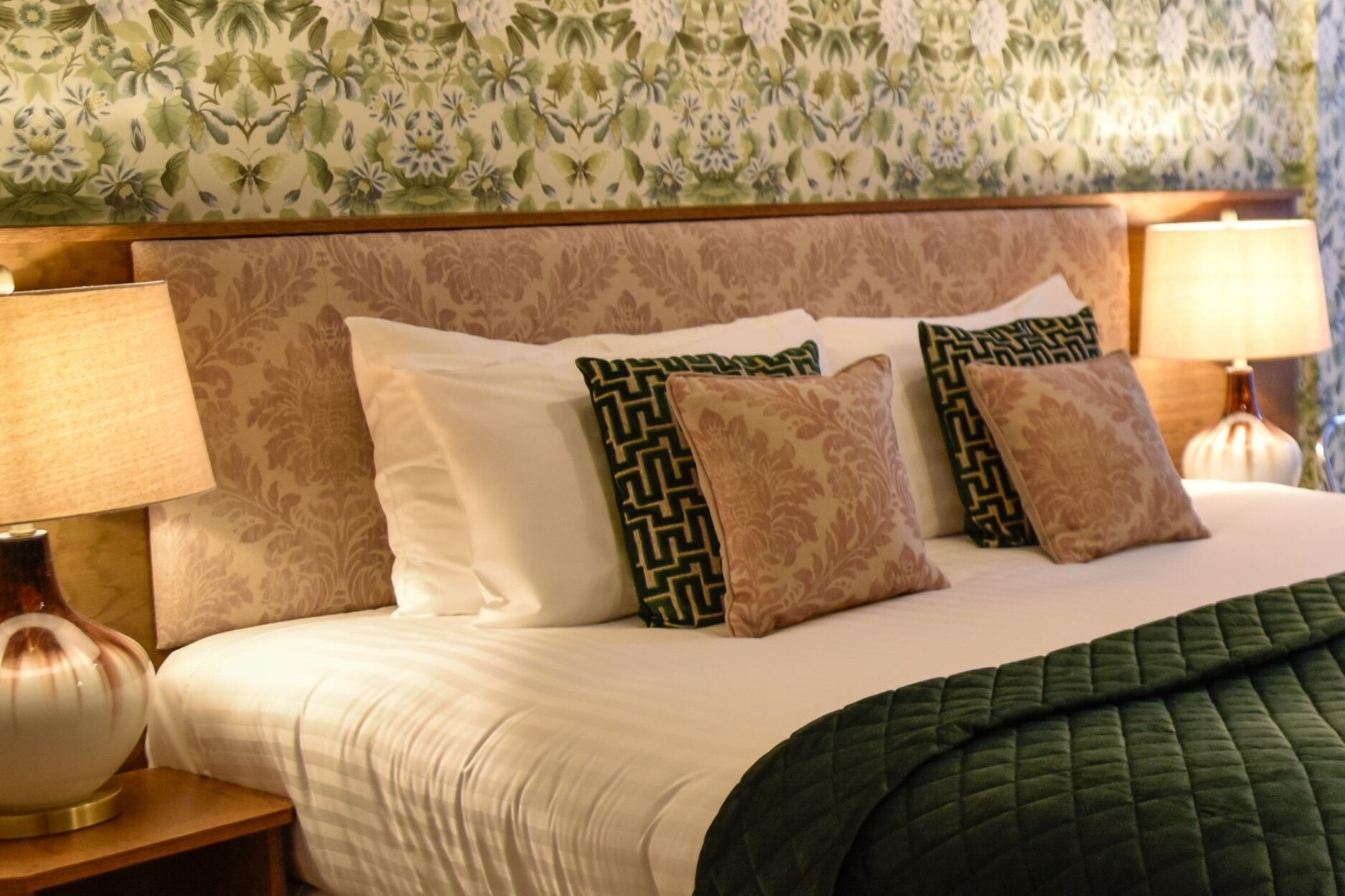 Close up shot of the accessible room bead, headboard, decorative cushions and decorative floral wallpaper.