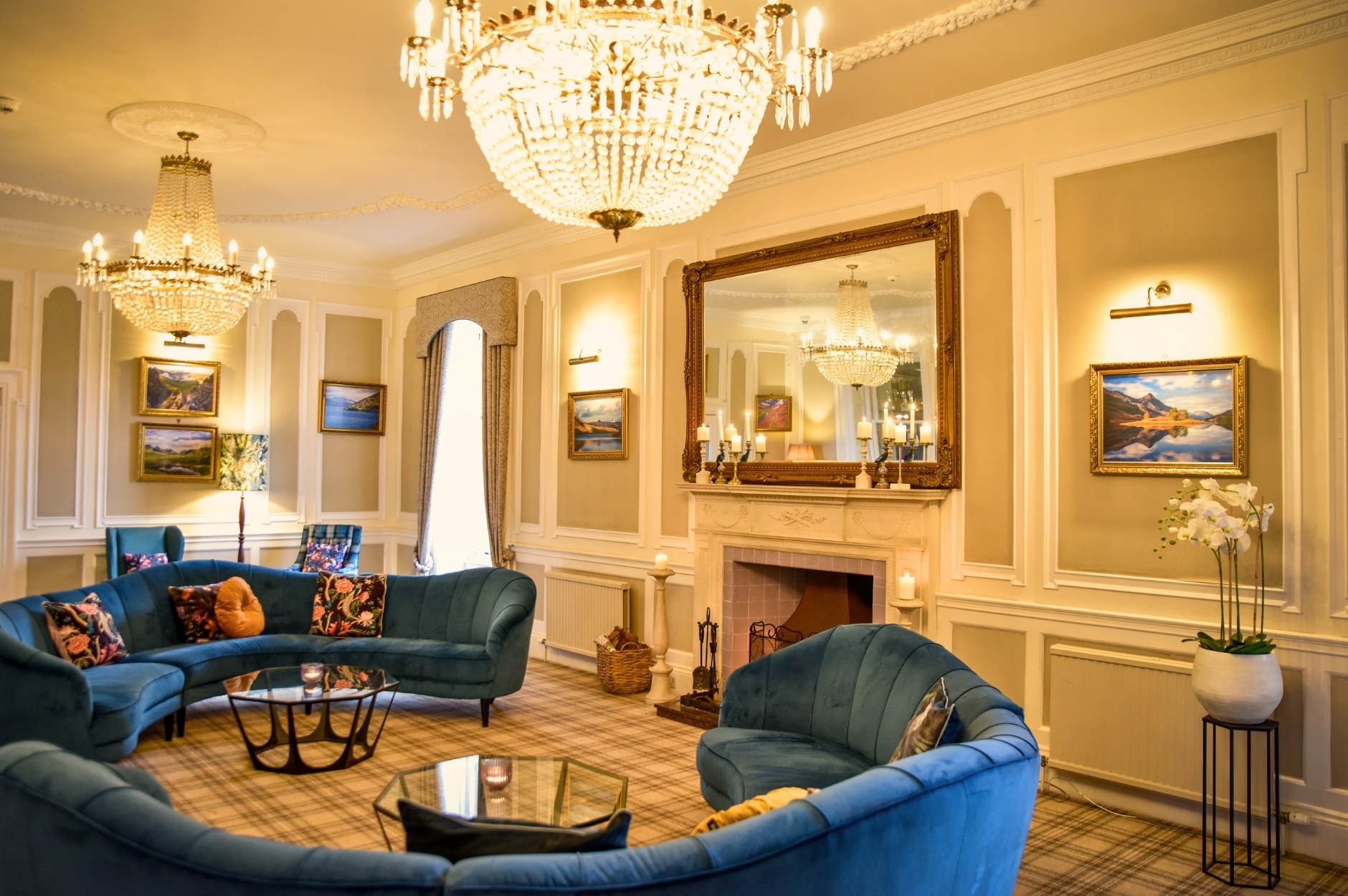 Shot of the beautiful Glenesk Hotel Chandalier Lounge with luxurious blue velvet sofas, two large chandeliers, fireplace and large mirror