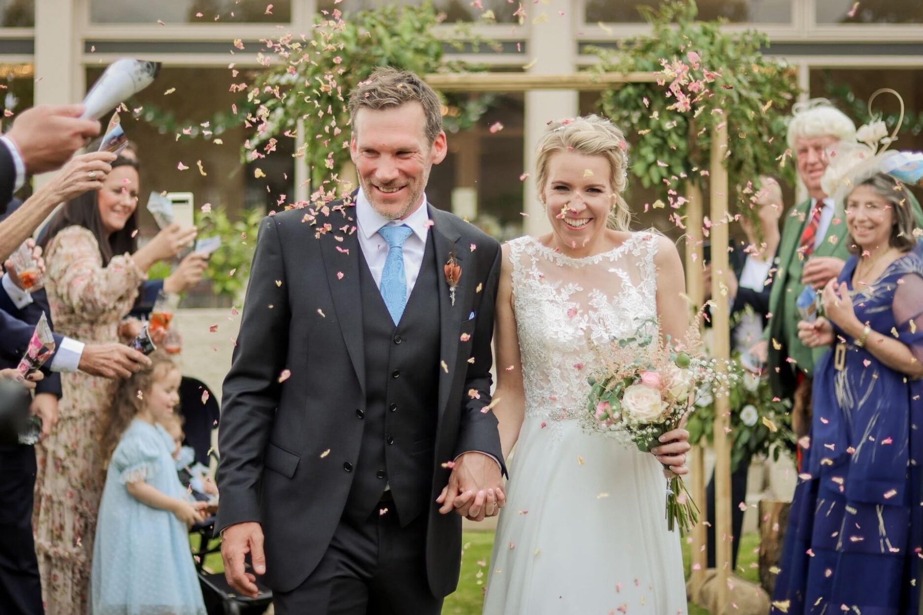 Bride and Groom walking under an arch and being sprinkled with confetti by wedding guests in garden at Glenesk Hotel Angus