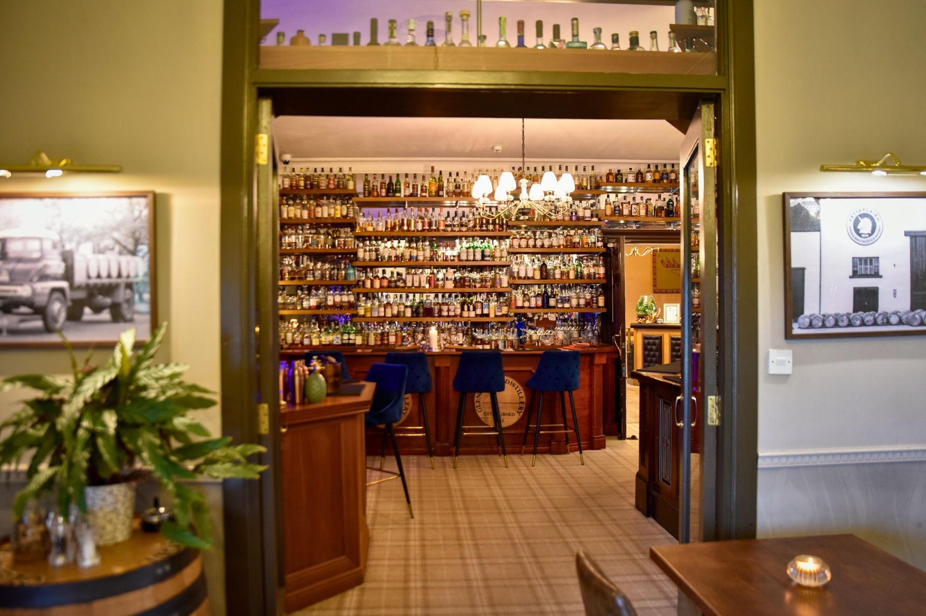 View into the whisky bar at the Glenesk Hotel Angus. Glass doors open to the bar area showing the barwith blue velvet bar stool. Over 500 bottles of whisky behind the bar.